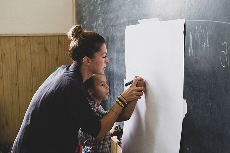 photo of teacher helping a child write on the chalkboard